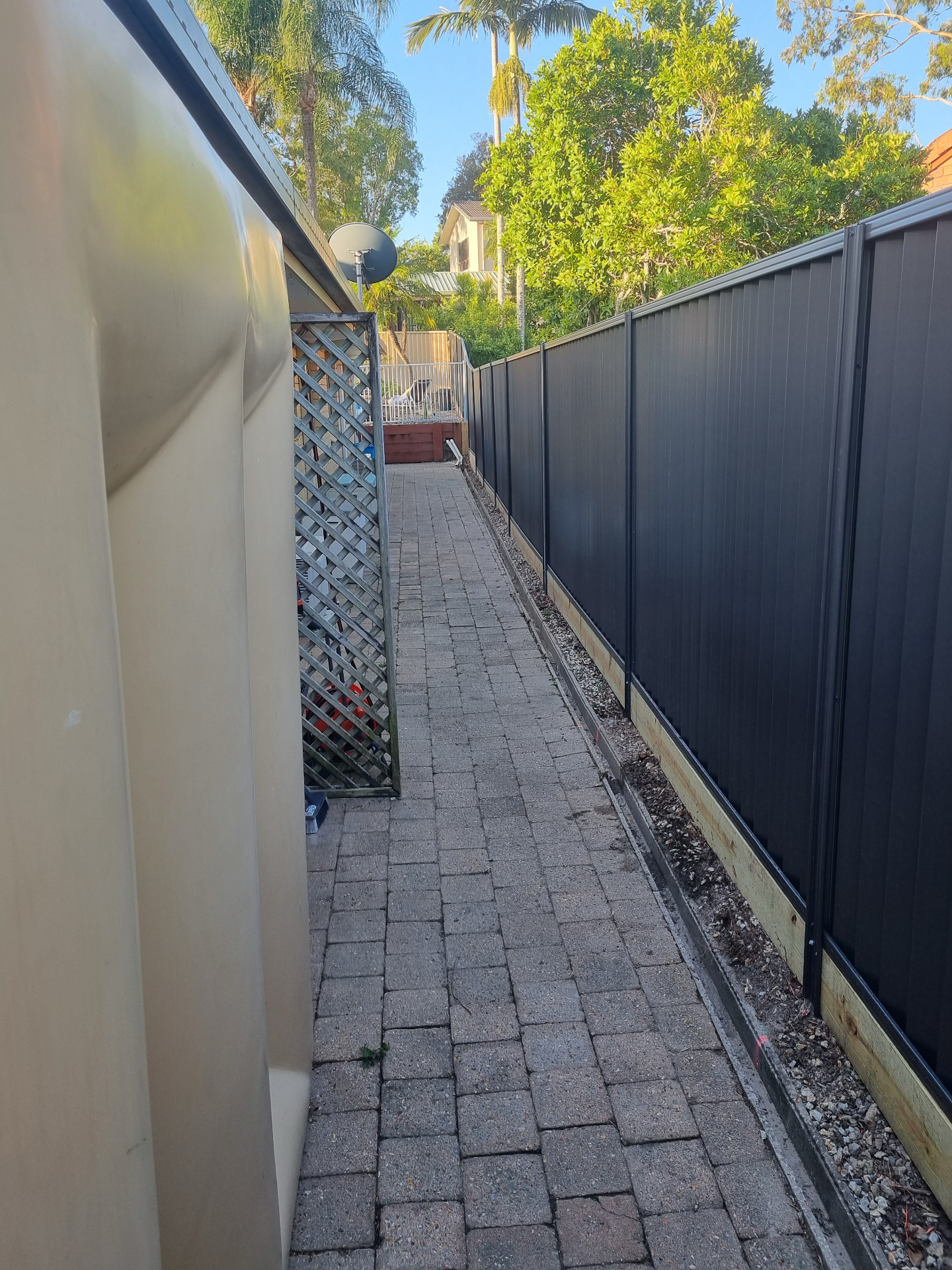 Dark Colorbond fence along a narrow paved side path with neat install line.