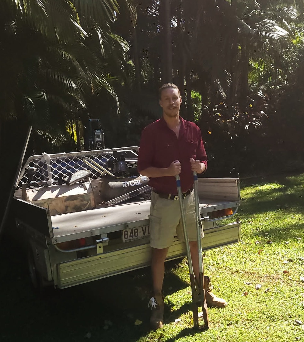 Oliver, owner of Ridgeback Fences, standing with post-hole diggers beside his work trailer.